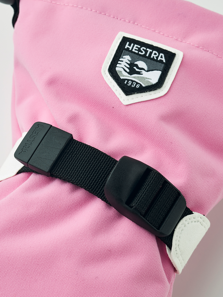 Nærbilde av logo og svart håndleddsrem på rosa Hestra Fjellvotten Jr.